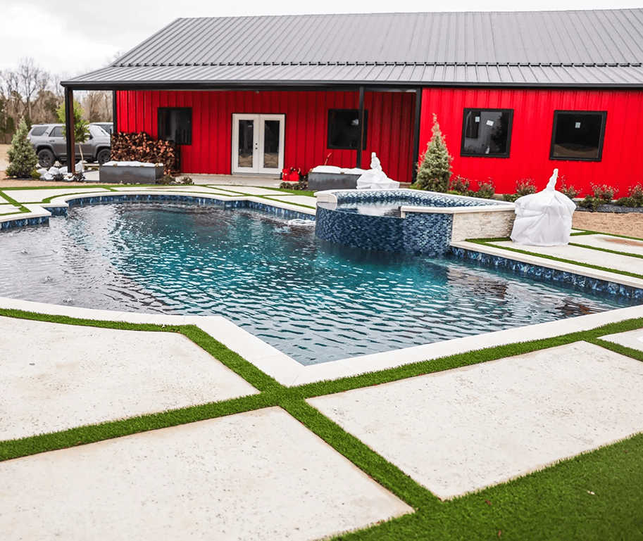 A pool with a red building and grass around it