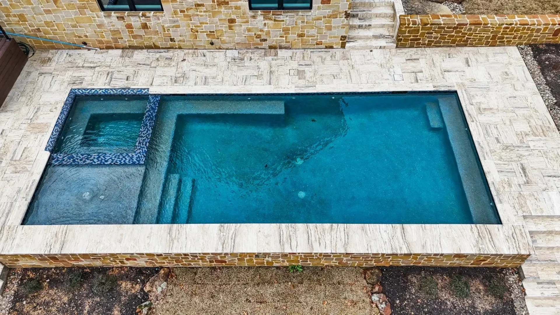 A pool with a stone wall and a blue tile surround.